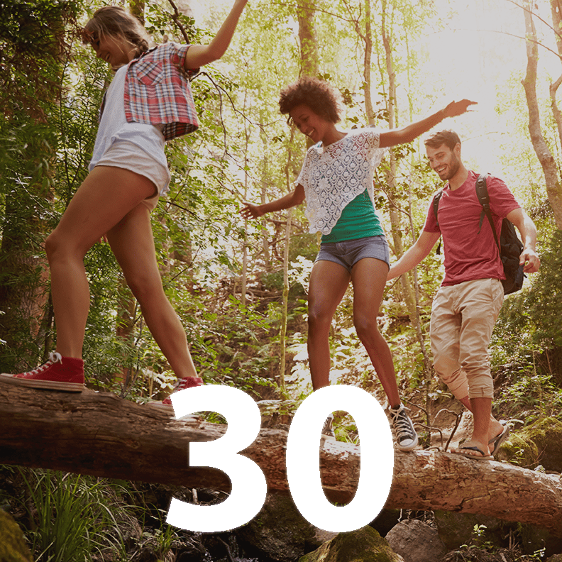 Three people walk along a fallen tree in a forest. Super-imposed is the number 30